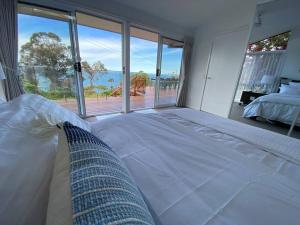 a white bed in a bedroom with a view of the ocean at ELEGANT LUXURY, STUNNING SEA VIEWS-see whales pass in Avoca Beach