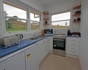 a kitchen with white cabinets and a sink and two windows at Hill Cottage Hahndorf in Hahndorf
