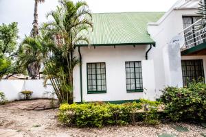 a white house with a green roof and palm trees at The Cottage in Rustenburg