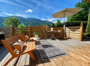 une terrasse en bois avec une table et un parasol dans l'établissement Androsace Appartement dans Chalet bois avec Jacuzzi privatif Terrasse et Vue Montagne, à Les Villards-sur-Thônes
