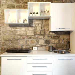a kitchen with white cabinets and a stone wall at Ikuvium Home in Gubbio
