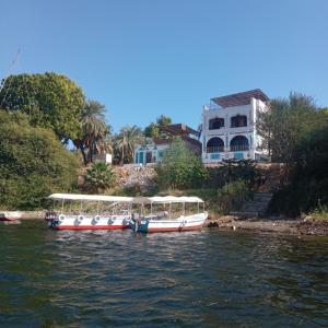 two boats are docked on a river with houses at Golden nubian guesthouse in Aswan