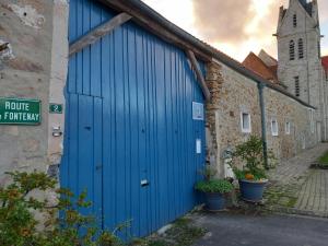 una puerta azul en el lateral de un edificio con una iglesia en La Bord de Mer (au Portail Bleu), en Châtres