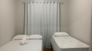 two twin beds in a room with white curtains at HOSTEL ECONOMIC DIVINOPOLIS in Divinópolis