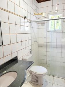 a white tiled bathroom with a toilet and a sink at Casa de praia / piscina in Santa Cruz Cabrália