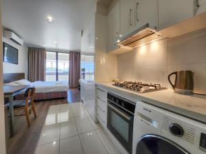 Exodus Dandenong Apartment Hotel في داندينونج: مطبخ مع موقد فرن علوي بجوار سرير