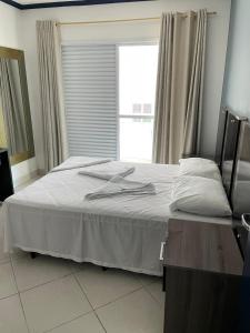 um quarto com uma cama com lençóis brancos e uma janela em Apartamentos Primavera Guarujá no Guarujá