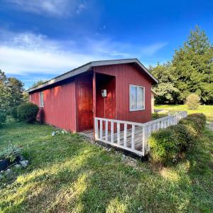 a red house with a white fence in the grass at Cabañas y Hospedaje Parque los Volcanes in Llanquihue