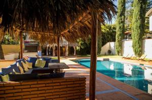 a swimming pool with a blue couch and a straw umbrella at Hotel Casa Yunenisa in Oaxaca City