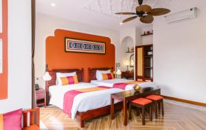 a bedroom with two beds and a desk and a table at De'Colore Villa Hoi An in Hoi An