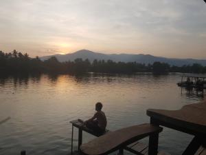 a man sitting on a bench in front of a lake at The Hideaway in Kampot