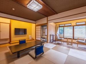 Atami Onsen Yamaki Ryokan في أتامي: غرفة مع طاولة وكراسي وتلفزيون