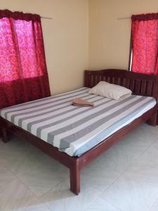 Cama de madera en habitación con cortinas rojas en Akoya Beach Park and Cottages en Locaroc