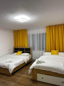 two beds in a room with yellow curtains at Vila AliBi Valiug - 200m from Ponton Casa Baraj in Văliug