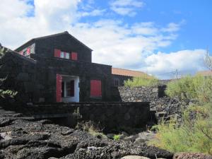 Casa negra con ventanas rojas y pared de piedra. en Casa do Jardim de Lava, en Arcos