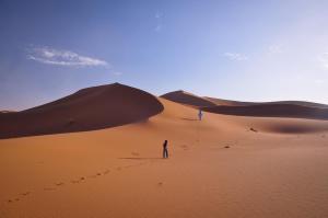 un hombre parado en una duna de arena en el desierto en Erg Chegaga Lodge, en Mhamid