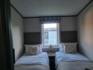 two beds in a small room with a window at Mawgan Pads Lazy Days Lodge in Mawgan Porth