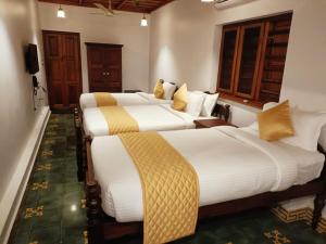 two beds in a hotel room with white and yellow pillows at Kalappura Farm House Heritage in Ottappālam