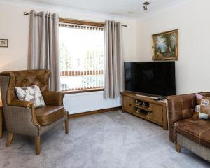 ein Wohnzimmer mit einem TV, einem Sofa und einem Stuhl in der Unterkunft No27 Willowbank in Dunkeld