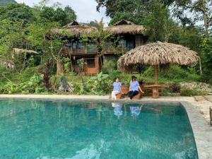 two people sitting on the edge of a swimming pool at PuLuong BamBoo in Hương Bá Thước