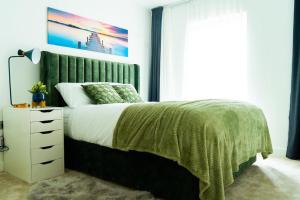 a bedroom with a bed with a green blanket and a dresser at Lavish 2 Bedroom Apartment in Colindale