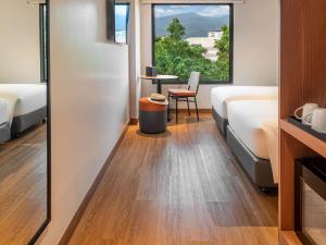 um quarto com duas camas e uma mesa e uma janela em ibis Chiang Mai Nimman Journeyhub em Chiang Mai