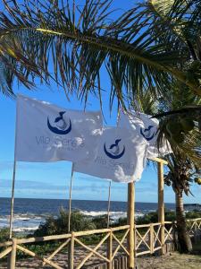two flags on the beach with the ocean in the background at Vila Sereia Caraiva in Caraíva