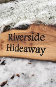 un cartello di legno che legge nascondiglio lungo il fiume sulla neve di Riverside Hideaway a Kincraig