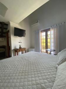 a bedroom with a large white bed and a television at Pousada Banzay in Paraty