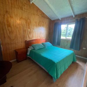 a bedroom with a bed with a blue comforter and a window at Cabañas y Hospedaje Parque los Volcanes in Llanquihue