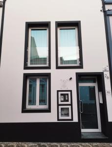 a white building with four windows and a door at Santa Alegria Hostel in Ponta Delgada