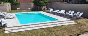 una piscina con sillas blancas y un montón de plantas en Hotel El Velero, en Villa Gesell