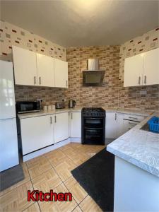 - une cuisine avec des placards blancs et une cuisinière noire dans l'établissement Cheerful 2 bedroom mid terrace house in BD2, à Bradford