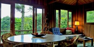 a living room with a table and chairs and windows at Pousada Sitio Gan Eden in Visconde De Maua