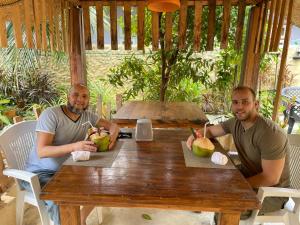 two men sitting at a wooden table with coconuts at Mathiveri Thundi Inn in Mathiveri