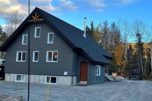 ein großes schwarzes Haus mit einer roten Tür in der Unterkunft Hébergement paisible à la montagne in LʼAnse-Saint-Jean