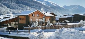 una cabaña de madera en la nieve con montañas en el fondo en Hotel Piccolo Tibet, en Livigno