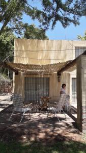 eine Person, die vor einem Gebäude auf Stühlen sitzt in der Unterkunft COMPLEJO DRUMMOND en el Camino del Vino in Ciudad Lujan de Cuyo