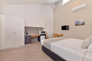 a white bedroom with a bed and a kitchen at Tathra Beach House Holiday Apartments in Tathra