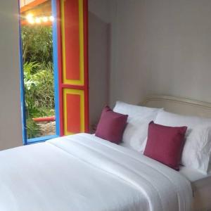 a white bed with two red pillows and a window at CASA DE CAMPO VILLA OLI!! - Un paraiso natural en la ciudad in Villamaría