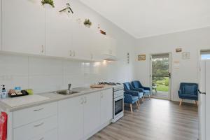 a white kitchen with white cabinets and blue chairs at Henkley Cottage 4 Daniel in Central Tilba