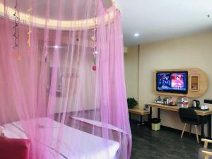 um quarto com cortinas cor-de-rosa e uma secretária com uma televisão em Thank Inn Chain Hotel henan zhengzhou xinzheng city north china road xuanyuan lake em Zhengzhou
