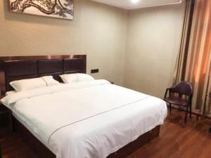 - une chambre avec un grand lit blanc et une chaise dans l'établissement JUN Hotels Jiangxi Yingtan Yujiang County Railway Station Store, à Yingtan