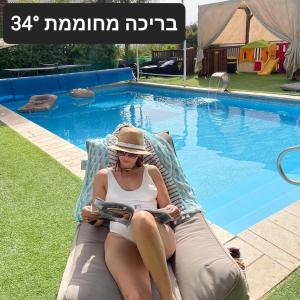 a woman sitting in a chair reading a book by a swimming pool at צימר חן בחד נס in Had Nes
