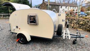a beige trailer is parked on the gravel at Wallace Teardrop Caravan for Hire from ElectricExplorers in Hawkshead