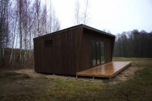 um pequeno edifício com um deque de madeira num campo em Riešutynė em Gražuliai