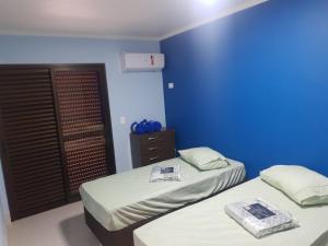 two beds in a room with a blue wall at Apartamento Duplex pé na areia em Boracéia in Bertioga