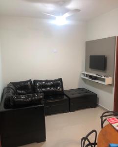 - un salon avec un canapé en cuir noir et une télévision à écran plat dans l'établissement Apartamento aconchegante em frente à praia., à Ubatuba
