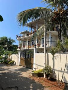 a white building with a fence and a palm tree at Habibi Hostel & Restaurant in Unawatuna