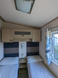 2 camas en una habitación pequeña con ventana en PEACEFUL HOMELY Caravan IN LOVELY CUL DE SAC Littlesea Haven Weymouth, en Weymouth